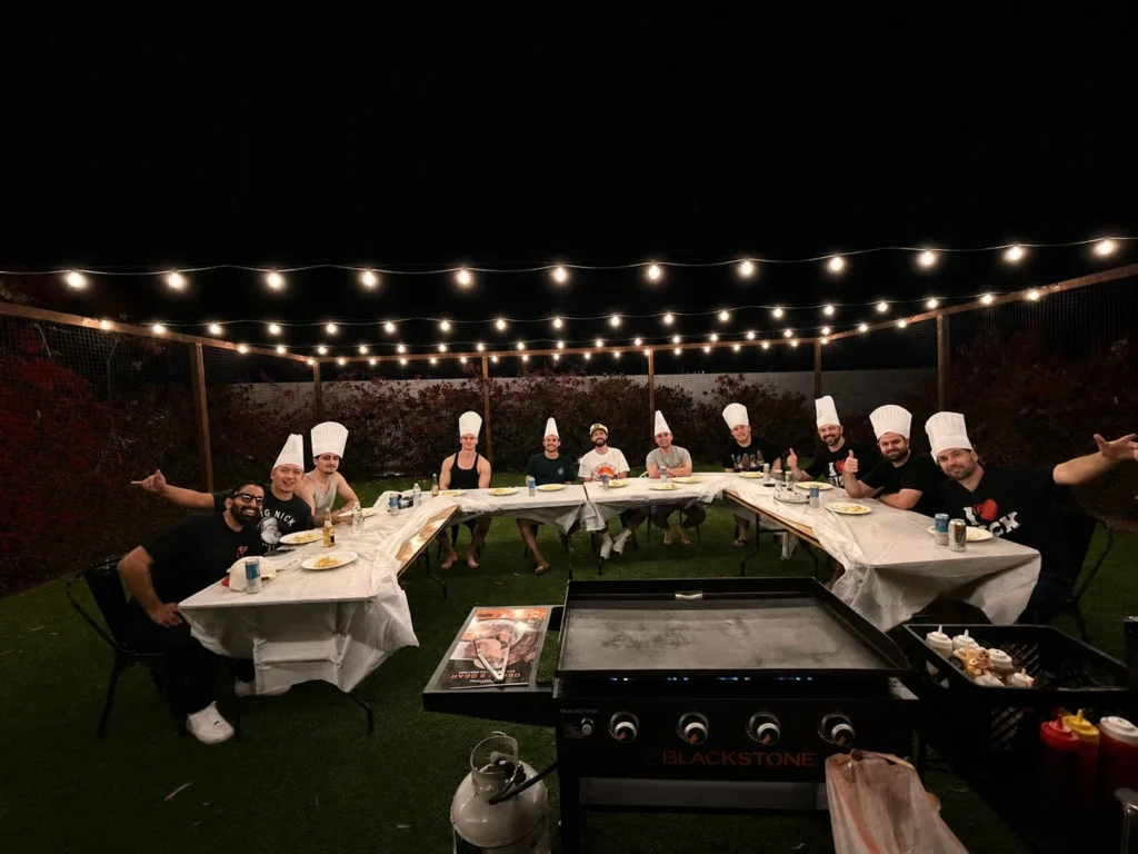 Guests wearing chef hats around an outdoor nighttime hibachi table